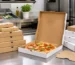 Boîtes à pizza kraft et blanches de plusieurs formats autour d’une pizza sur un poste d’emballage professionnel.